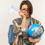 unpleased-young-student-girl-wearing-glasses-back-bag-holding-airplane-tickets-globe-isolated-white-background-with-copy-space