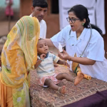 In a rural health care camp, a picture captures a crucial moment as a female doctor administers polio dosage to a child. The image highlights the efforts of medical professionals in preventing the spread of polio and protecting the health of young children in rural communities.